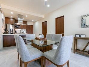 A modern kitchen with stainless steel appliances, a glass dining table with four grey upholstered chairs, and wooden cabinets.