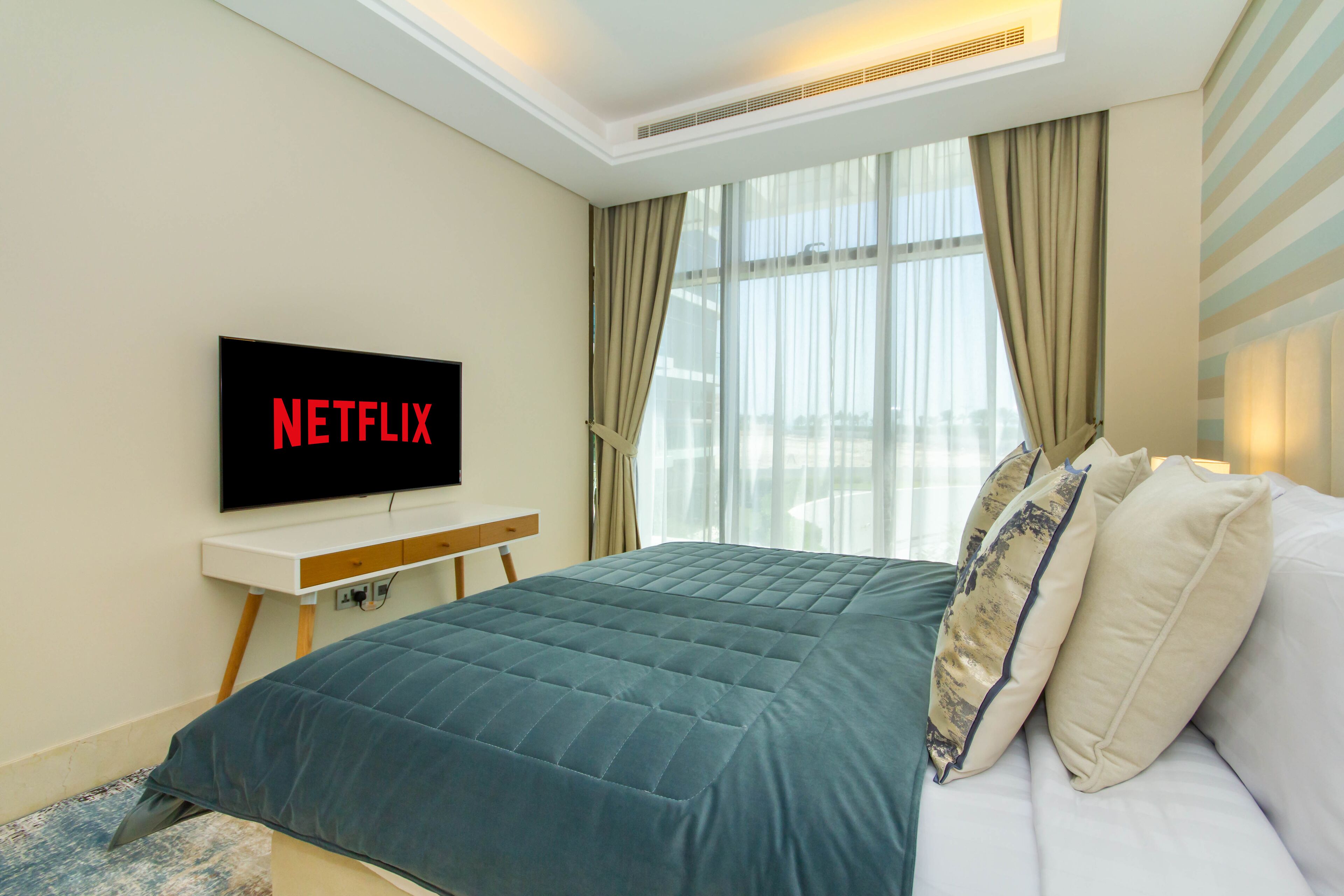 Une chambre d’hôtel moderne avec un grand lit, un téléviseur  à écran plat fixé au mur et une fenêtre agrémentée de rideaux légers.