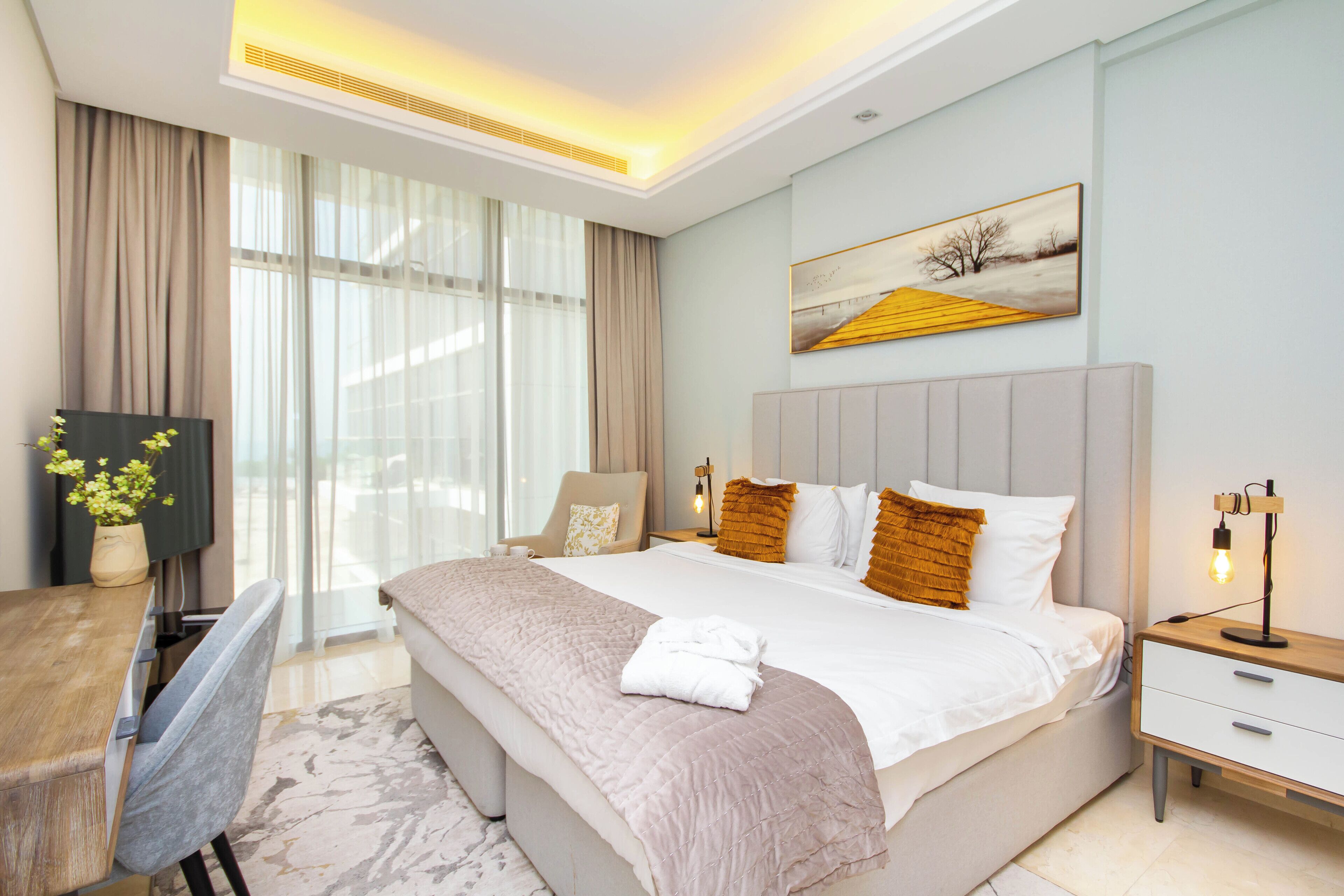 Une chambre d’hôtel moderne avec un grand lit, un bureau et une chaise. Il y a un tableau au mur et une fenêtre avec des rideaux.
