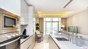 A modern kitchen with a built-in oven, a microwave, and a sink. There is a dining area with a sofa and a small table. - Bespoke Residences - Th8 Palm Jumeirah (Dubai)