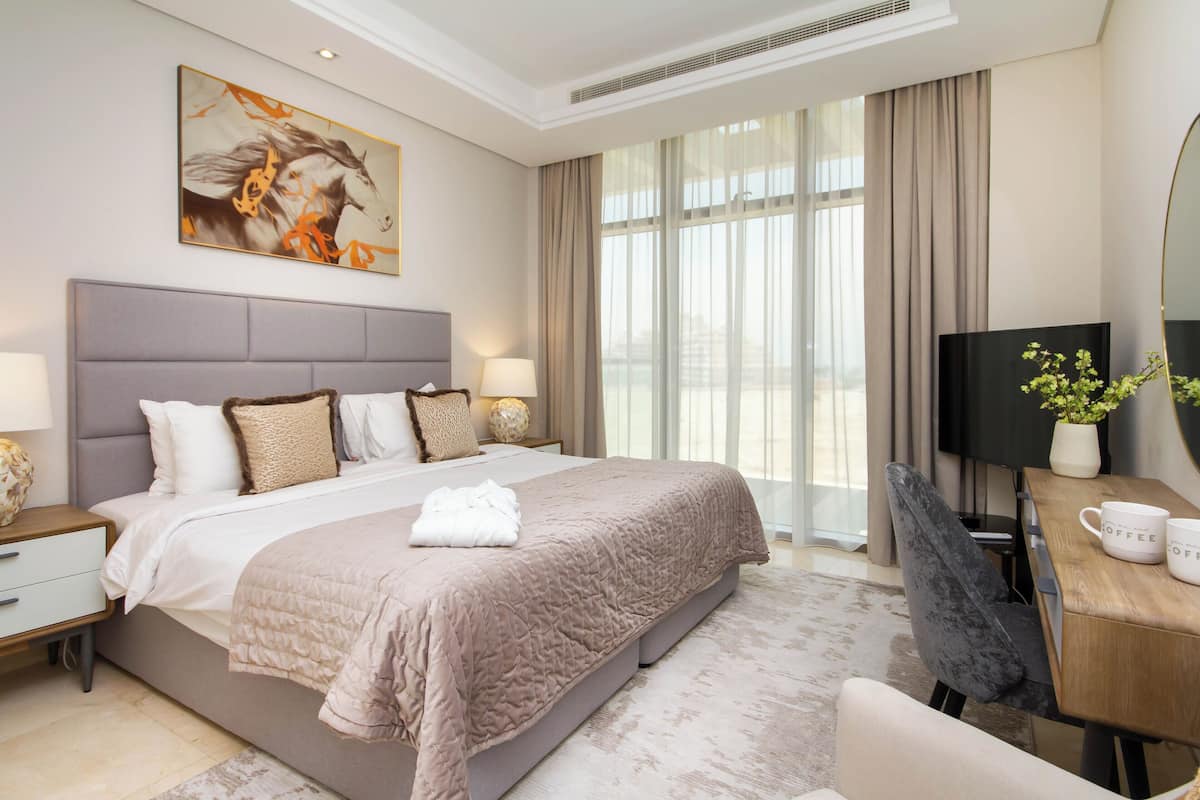 A modern hotel room with a large bed, a desk with a TV, and a window with curtains.
