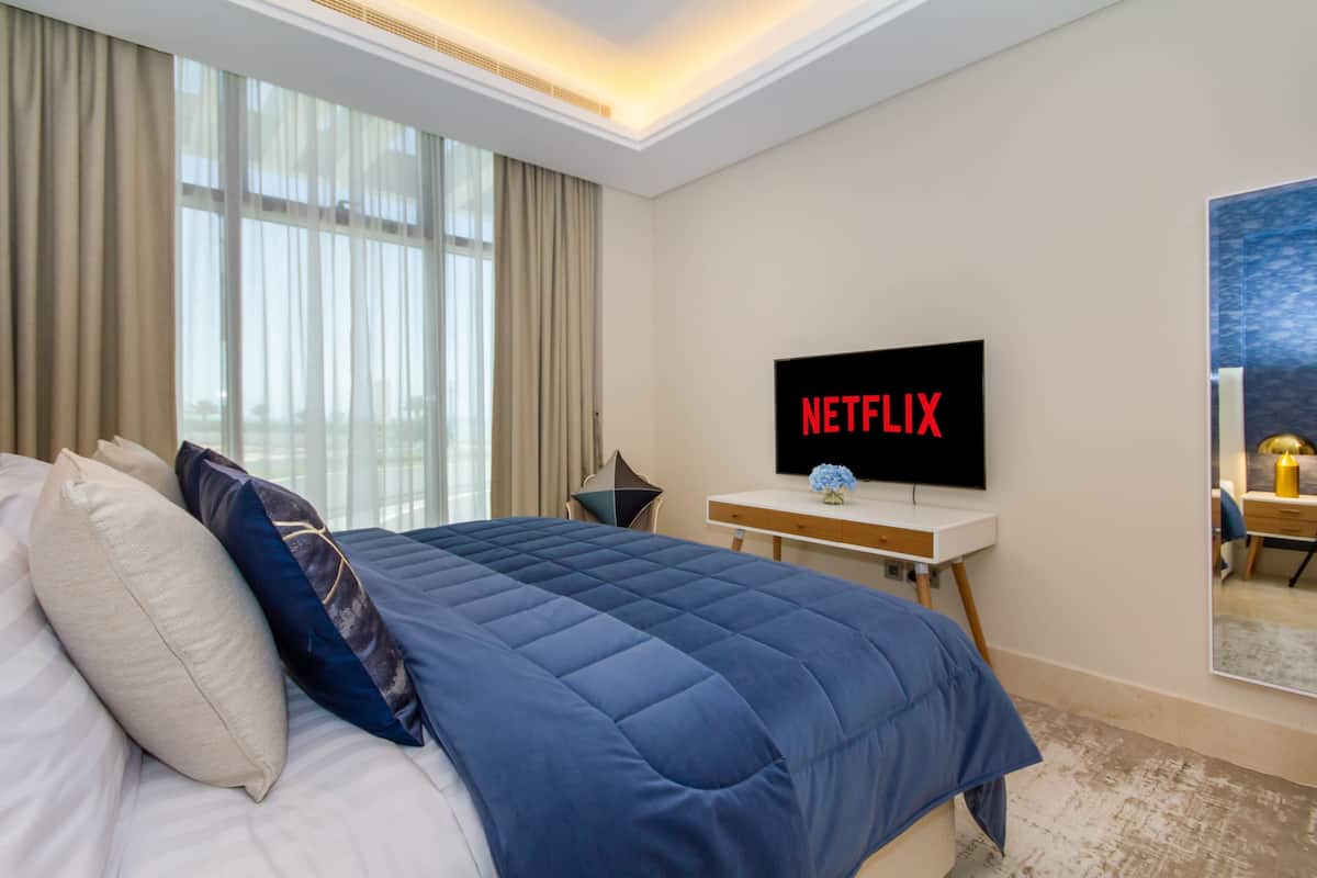 A hotel room with a large bed, a desk with a flat-screen TV, and a window with curtains.