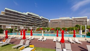 A hotel with a pool area featuring sun loungers and red umbrellas, surrounded by modern buildings. - Bespoke Residences - Th8 Palm Jumeirah (Dubai)