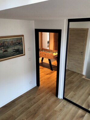 Enter a contemporary space with a hallway leading to a room featuring a foosball table and a framed harbor scene.