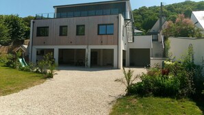 Une maison moderne à deux étages, dotée d’une allée couverte, d’un petit jardin et d’un escalier menant à l’étage supérieur.