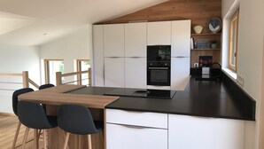 Une cuisine moderne avec des meubles blancs, un plan de travail noir et un four encastré. On y trouve une table à manger en bois avec quatre chaises.