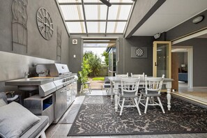 Enjoy al fresco dining in this outdoor kitchen area, featuring a grill and sink, a dining table, and a dartboard.