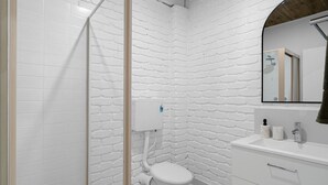 A bathroom with white brick walls, a white toilet, a sink with a mirror, and a shower area. - Moonah Shades Studio Rye - renovated with lovely garden - Spacious self contained studio, garden and fire pit (Rye)