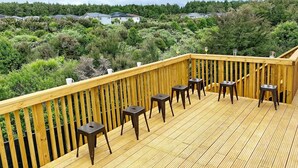 Eine Holzterrasse mit Geländer, mit einer Sitzgelegenheit, bestehend aus Hockern und einem Tisch.