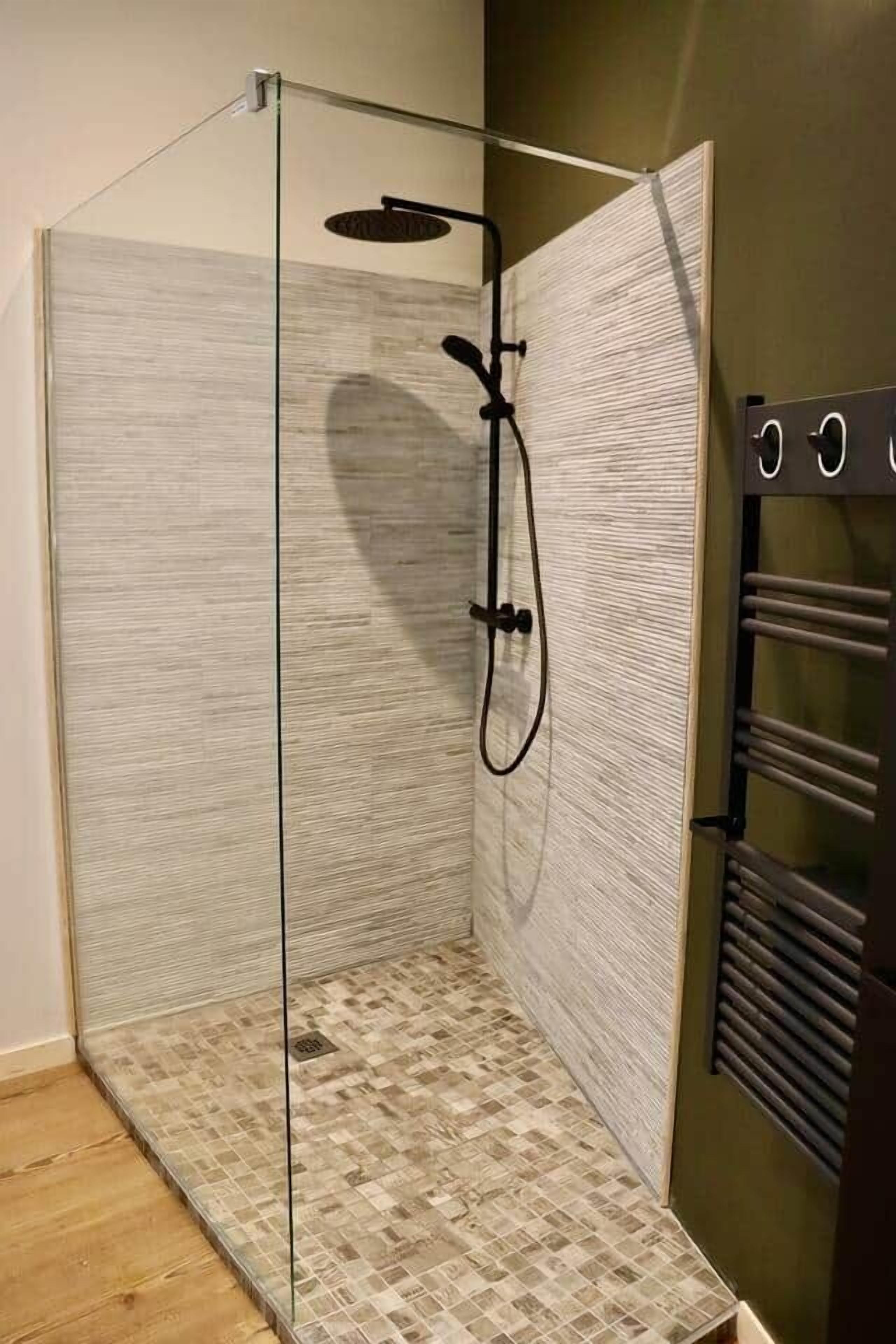 Une douche fermée par des parois de verre, avec un mur à texture et un sol carrelé.