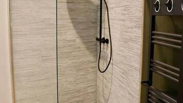 Une douche fermée par des parois de verre, avec un mur à texture et un sol carrelé.