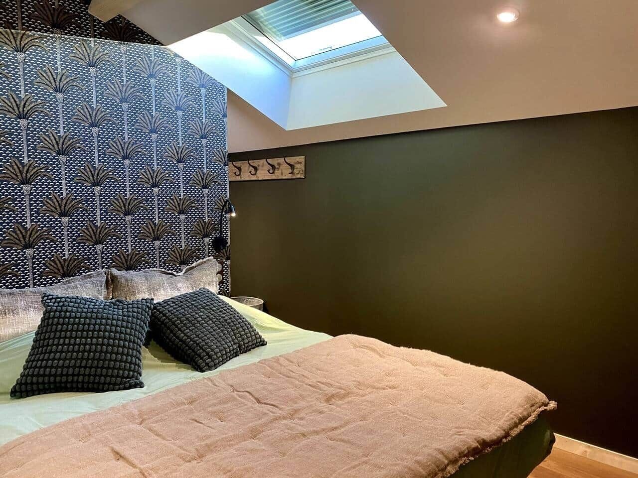 A bedroom with a skylight, a patterned headboard, and a bed with two pillows.