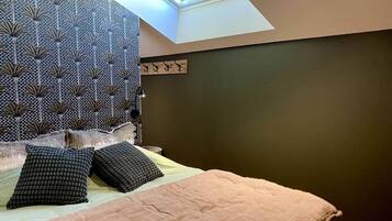 A bedroom with a skylight, a patterned headboard, and a bed with two pillows.