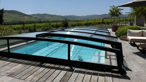 A pool area with multiple glass-enclosed pools, wooden decking, and a view of distant hills.