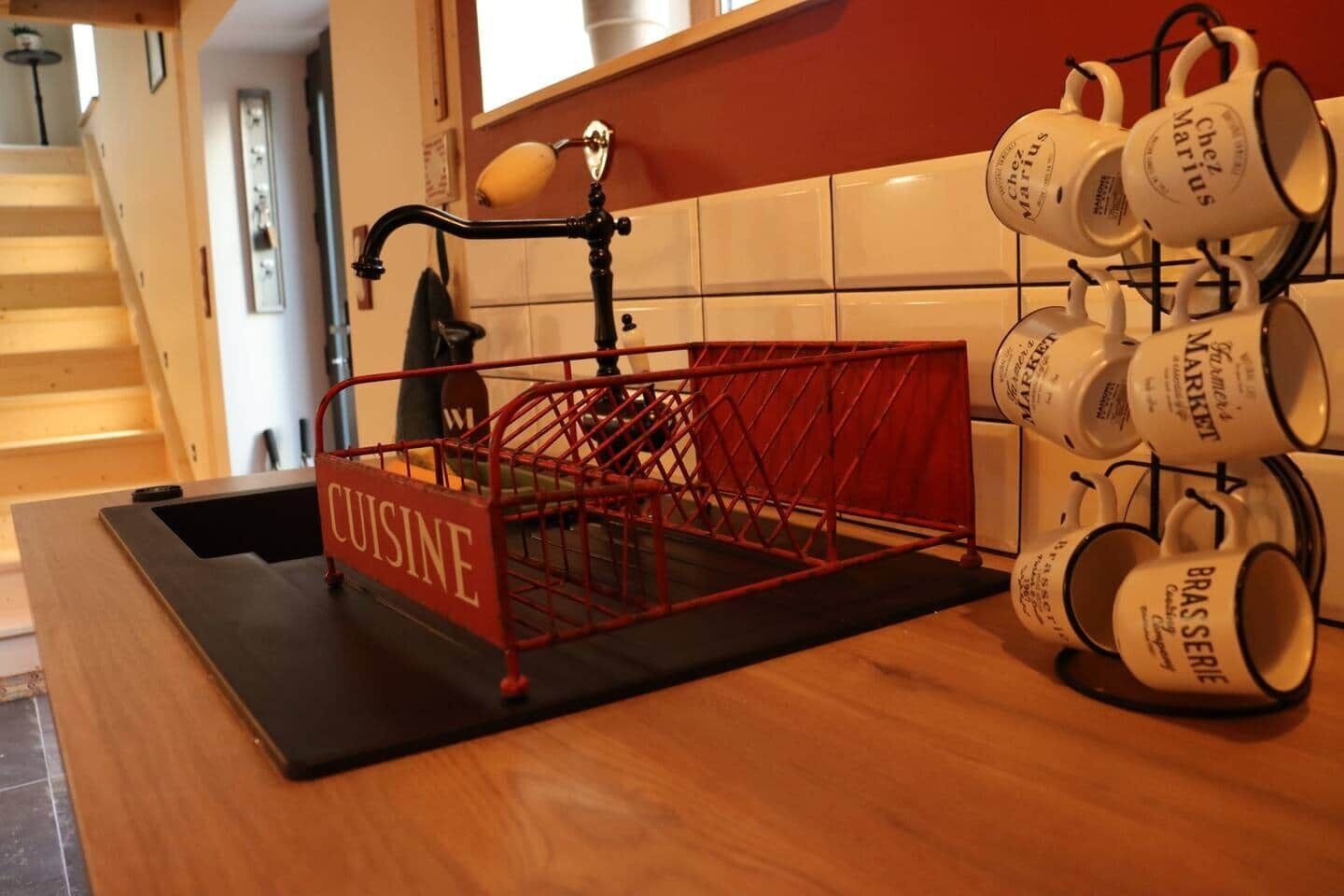 Un plan de travail de cuisine avec une étagère en métal rouge portant l’inscription « CUISINE » et une autre étagère avec des tasses blanches ornées de texte noir.
