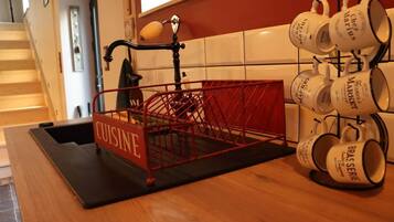 Un plan de travail de cuisine avec une étagère en métal rouge portant l’inscription « CUISINE » et une autre étagère avec des tasses blanches ornées de texte noir.