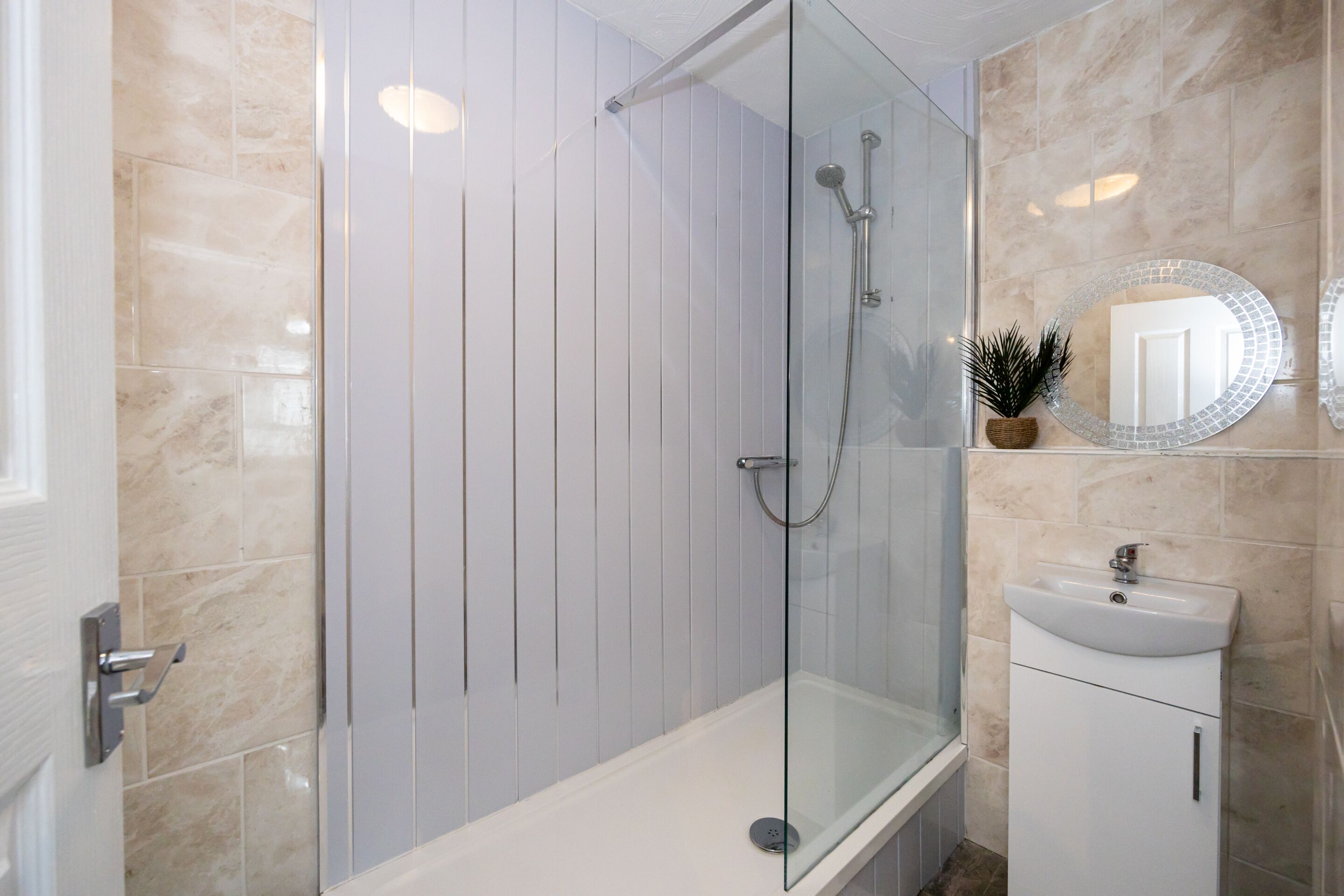 A modern bathroom with a glass-enclosed shower, a white sink, and a mirror with a mosaic frame.