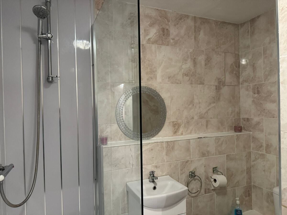 Une salle de bain moderne avec une douche à parois de verre, un lavabo avec un miroir au-dessus et des toilettes dotées d’un porte-serviettes en papier.