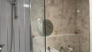 Une salle de bain moderne avec une douche à parois de verre, un lavabo avec un miroir au-dessus et des toilettes dotées d’un porte-serviettes en papier.