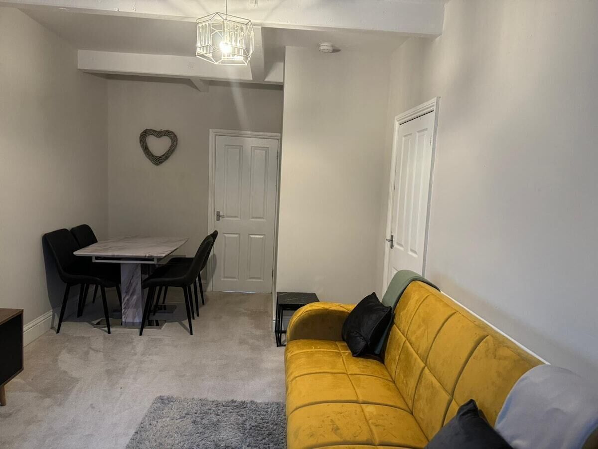 A compact living space with a dining table and chairs, a sofa, and a heart-shaped decoration on the wall.