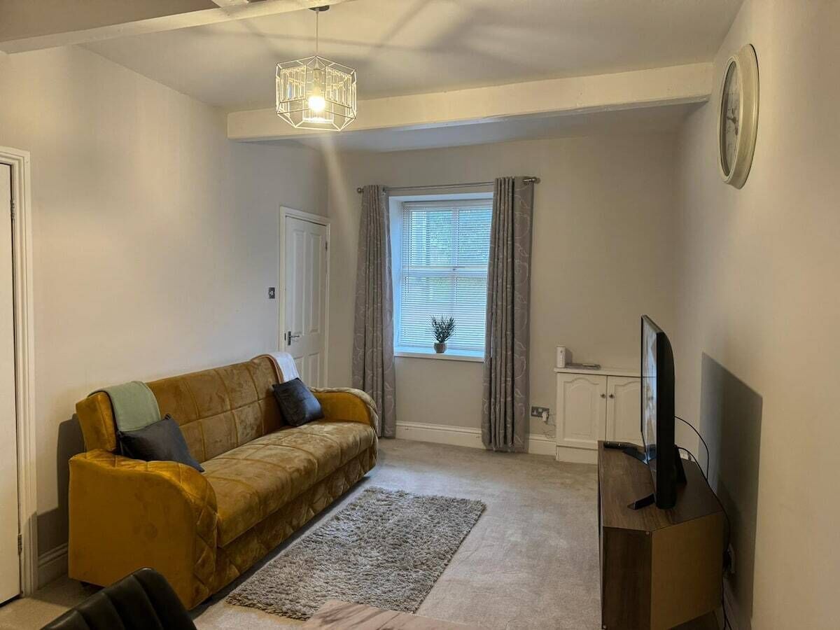A living room with a sofa, a television, a rug, a window with curtains, and a clock on the wall.