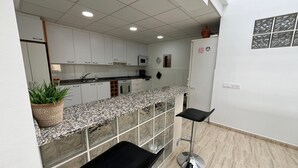 Eine moderne Küche mit weißen Schränken, Granit Arbeitsplatten und Edelstahlgeräten. Zwei schwarze Barhocker und ein Blumentopf sind vorhanden.
