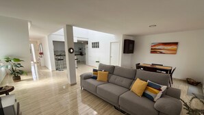Ein modernes Wohnzimmer mit grauem Sofa, einem Esstisch und einer Küche im Hintergrund.