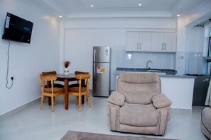 A compact living space with a dining area, a sofa, a kitchenette, and a flat-screen TV mounted on the wall.