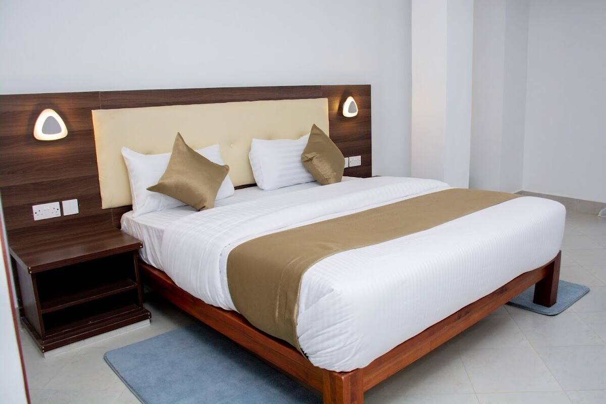Uma cama bem arrumada com cabeceira de madeira, mesa de cabeceira e tapete azul.