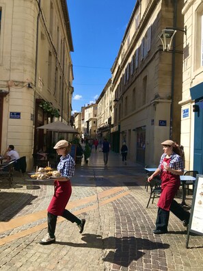 Une rue pavée bordée de bâtiments historiques, de terrasses et sous un ciel d’un bleu éclatant.