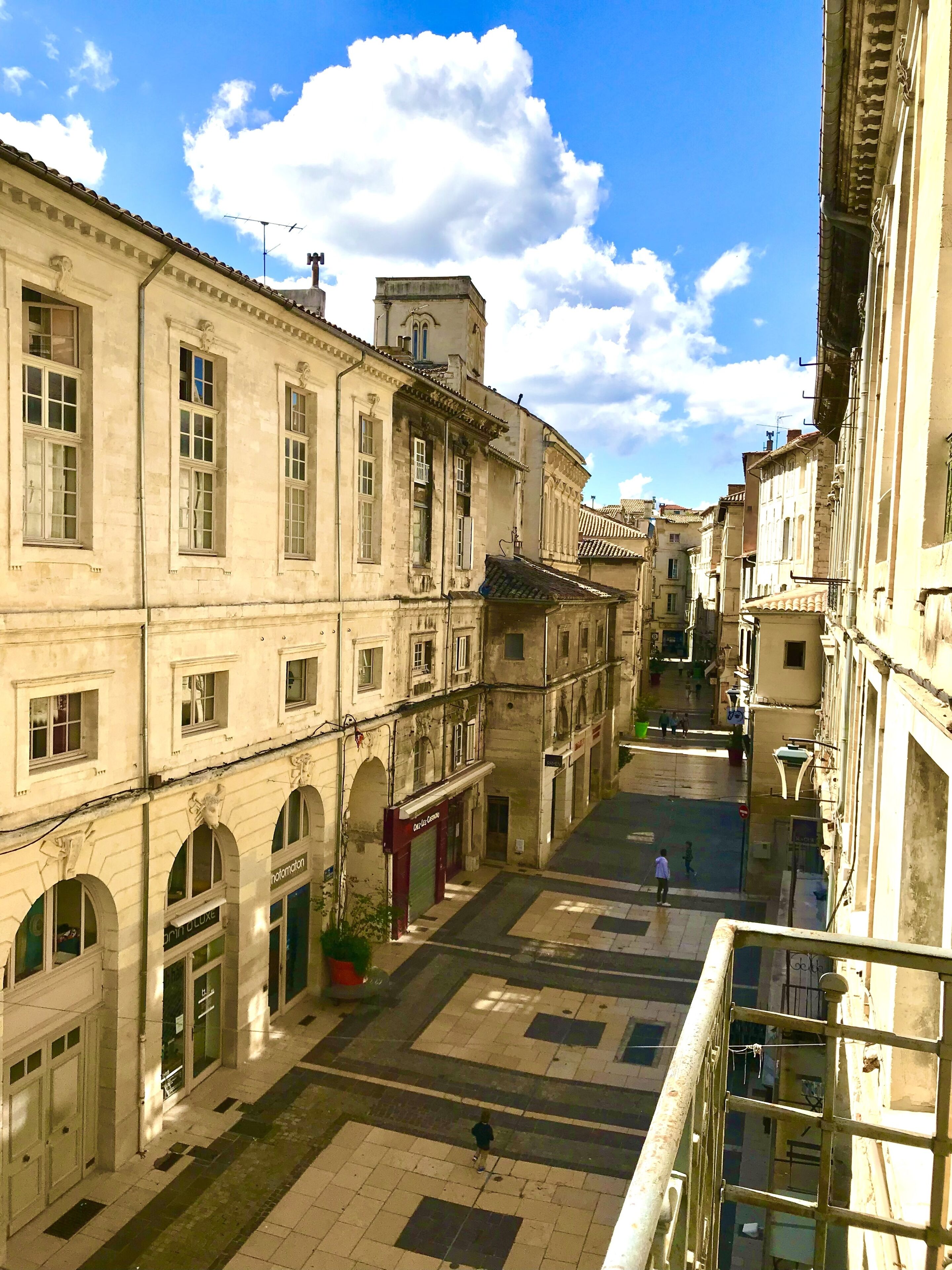 A courtyard with buildings on either side, featuring arched windows and a tiled floor.