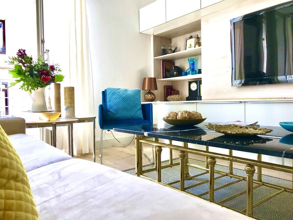 Un salon moderne avec un fauteuil bleu, une table basse et un téléviseur fixé au mur.