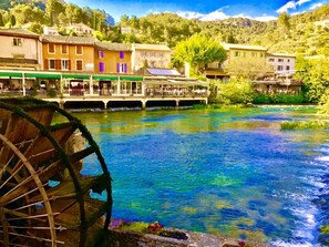 Une rivière avec une roue à eau, des bâtiments dotés de balcons et un pont.