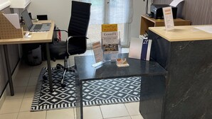 A reception area with a desk, chairs, a computer, and a poster on the wall. - Le Clos du Thoronet (Le Thoronet)