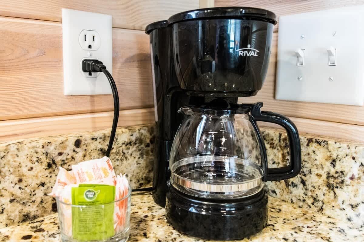 A black coffee maker on a granite countertop, connected to a power outlet.