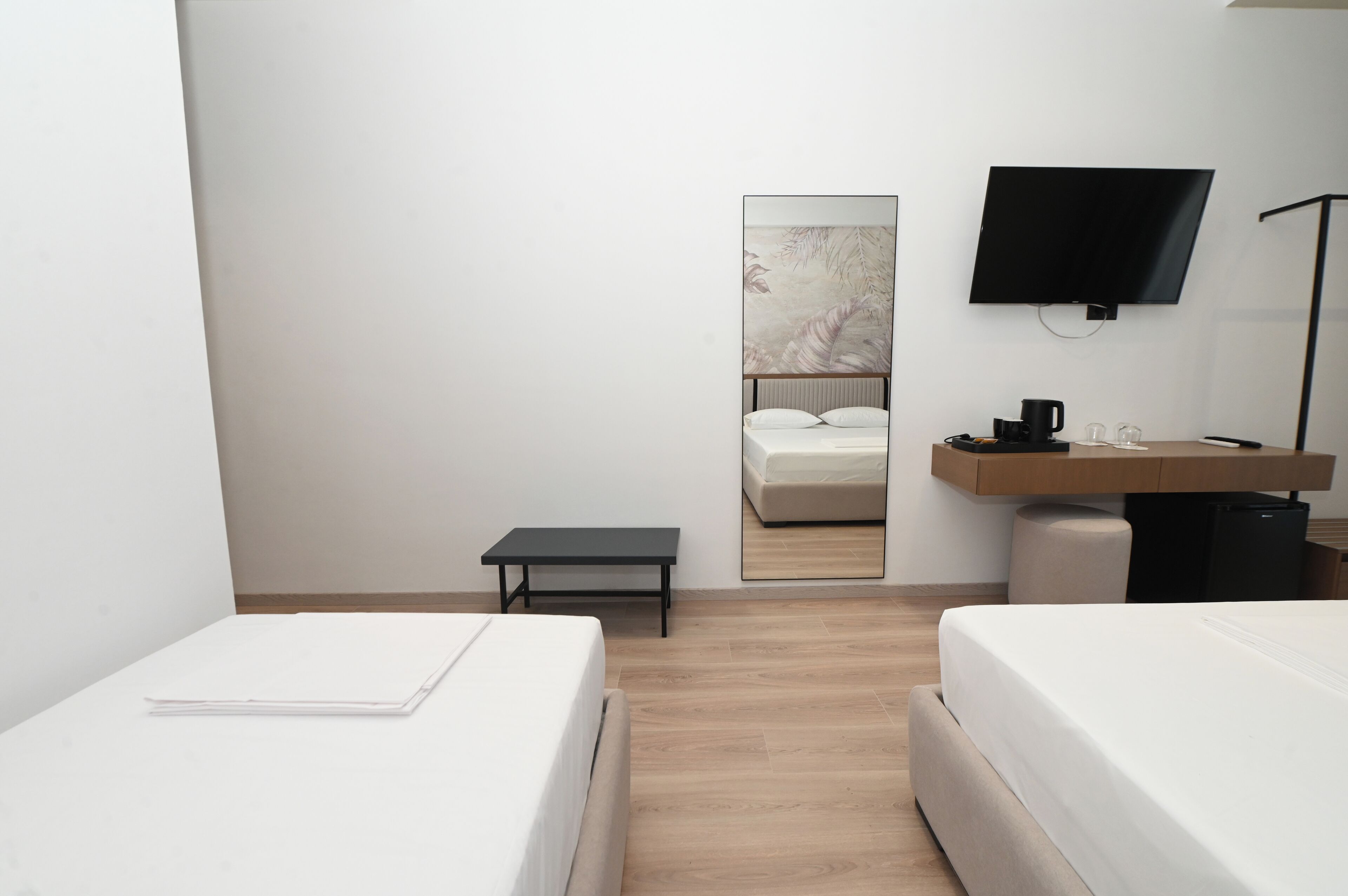 A hotel room with two beds, a small table, a mirror, a TV, and a coffee machine.