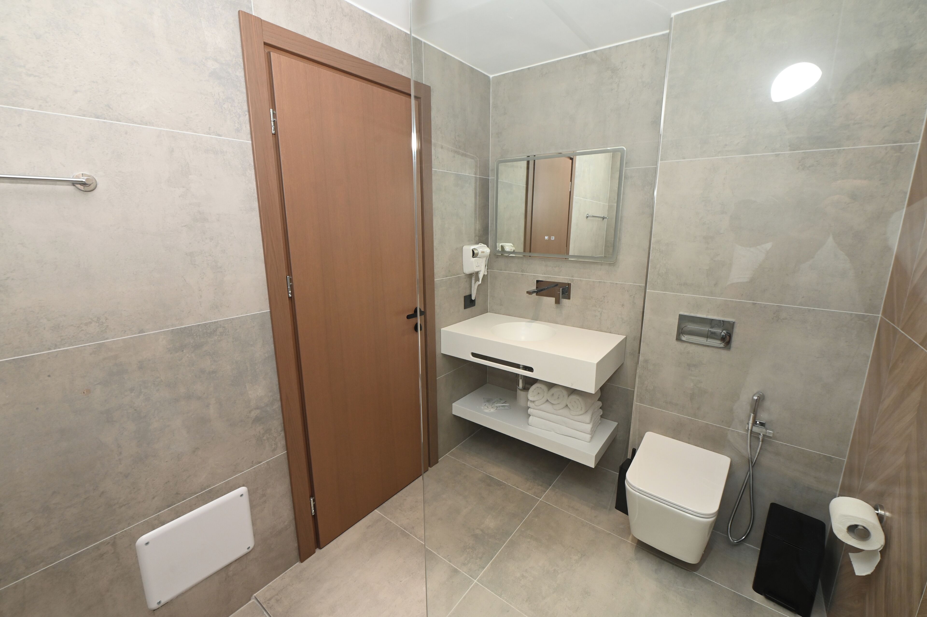 A bathroom with a wooden door, a white sink, a mirror, a toilet, and a shower.