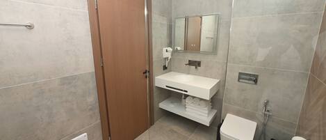 A bathroom with a wooden door, a white sink, a mirror, a toilet, and a shower.