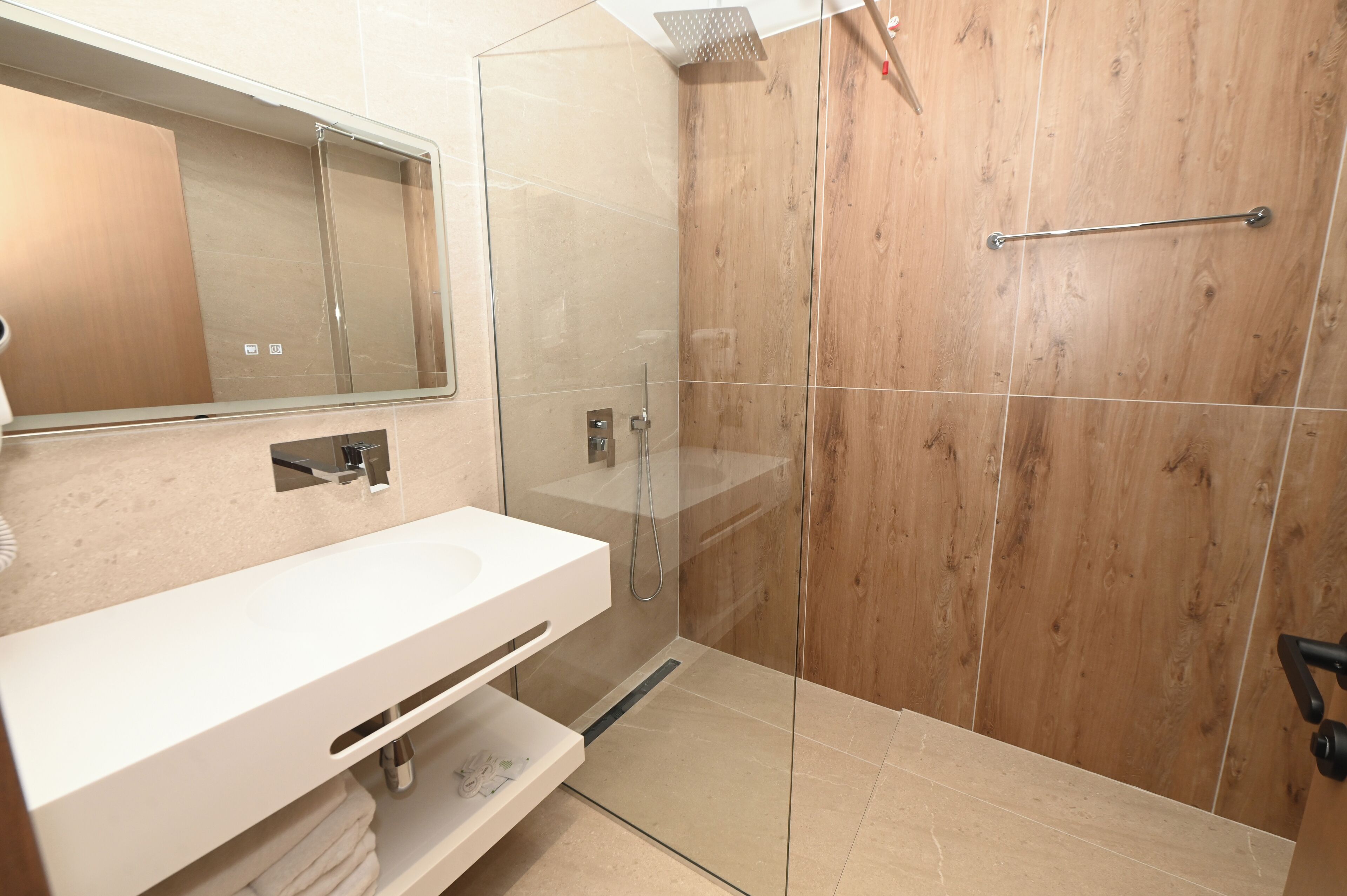 A modern bathroom with a glass-enclosed shower, a white vanity, and a wooden panel wall.