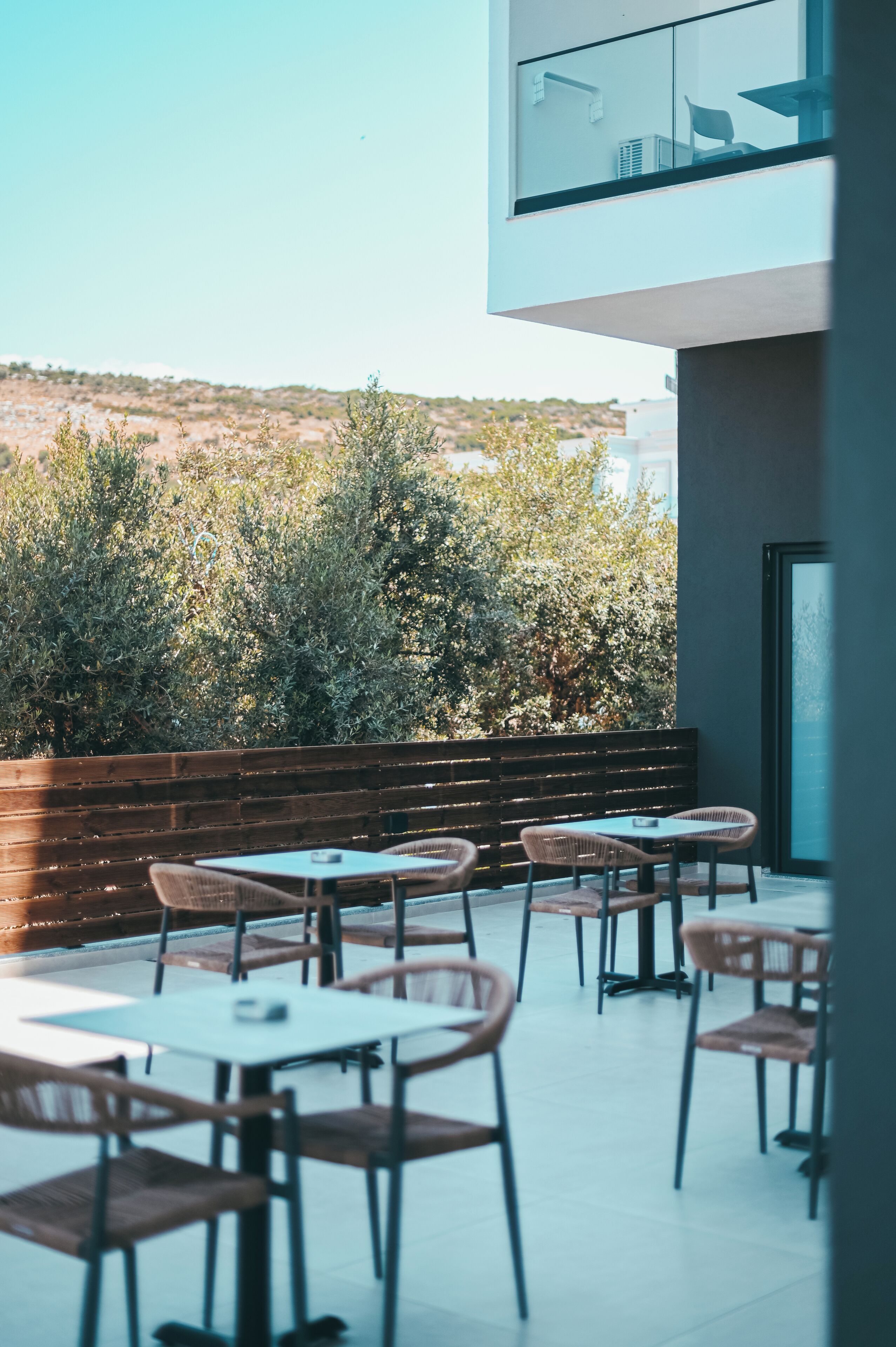 An outdoor seating area with tables and chairs, a wooden bench, and a view of a hilly landscape.