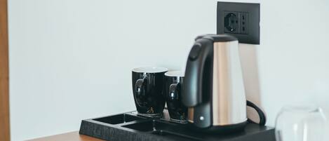 Une machine à café posée sur une table en bois, avec un verre d’eau et une tasse noire.