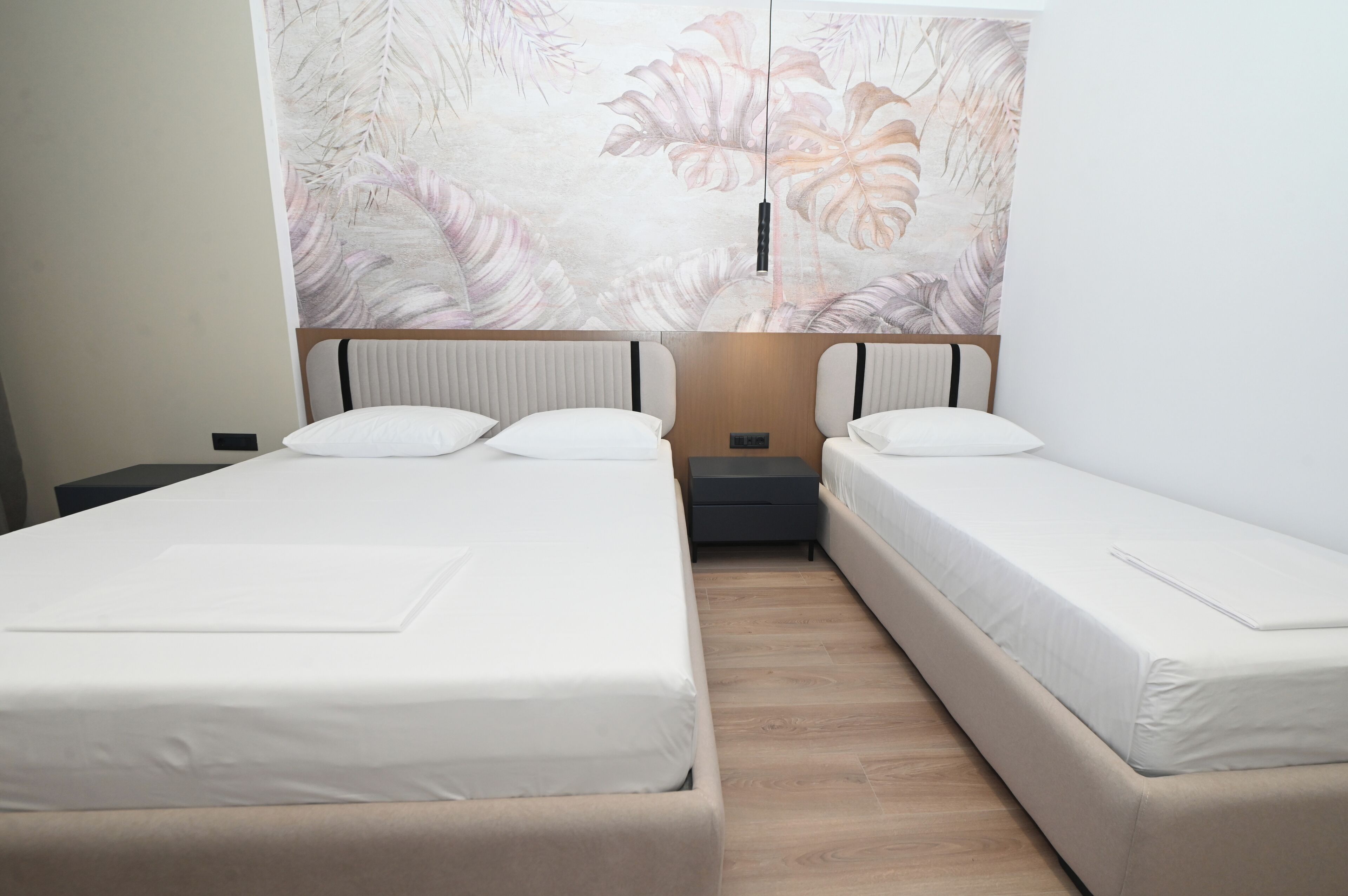 Une chambre double avec deux lits, une grande œuvre d’art à motifs floraux accrochée au mur et une petite table de chevet.