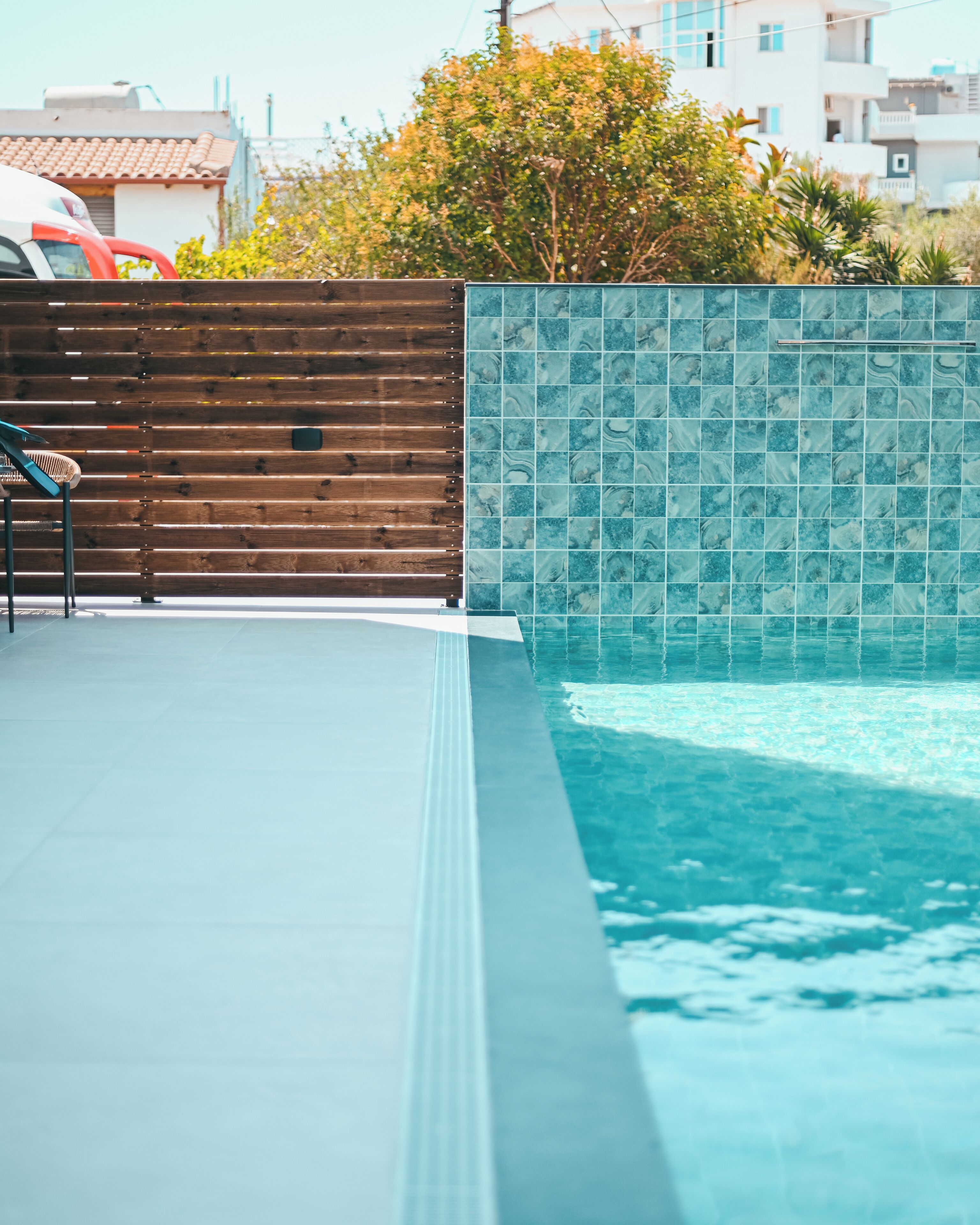 Une piscine entourée d’une clôture en bois et d’un mur carrelé, avec une terrasse également carrelée et une chaise.