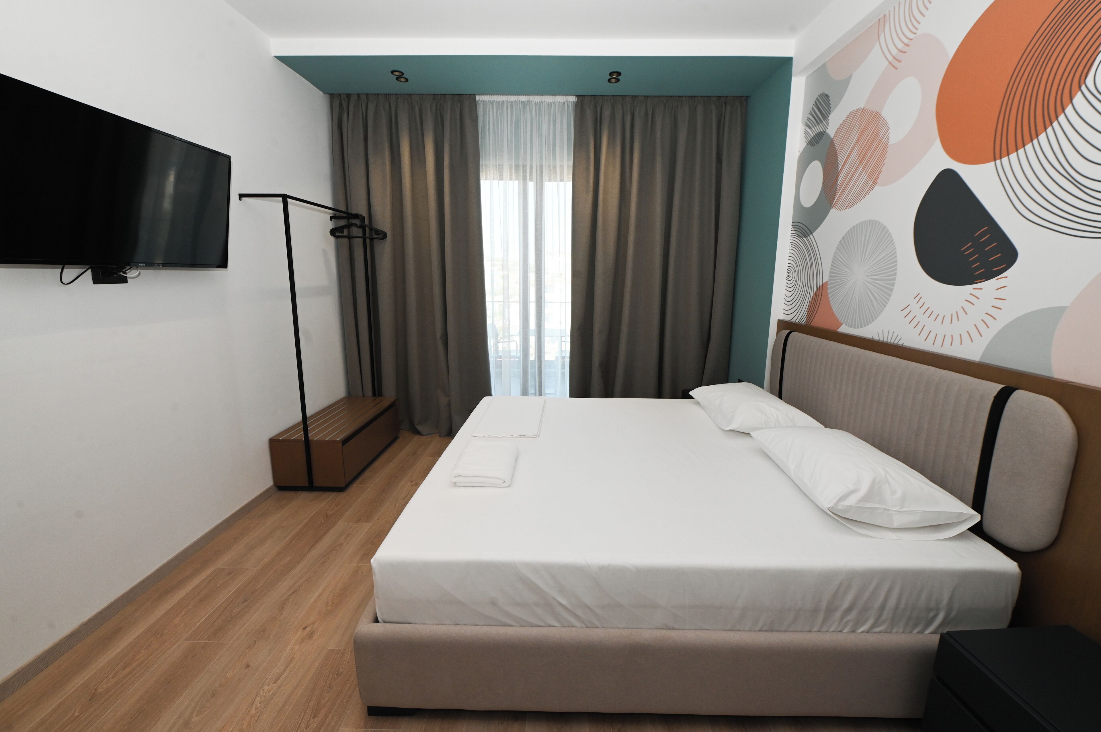 Una camera d'hotel moderna con un letto grande, una televisione a schermo piatto fissata al muro e vista sulla città dalla finestra.