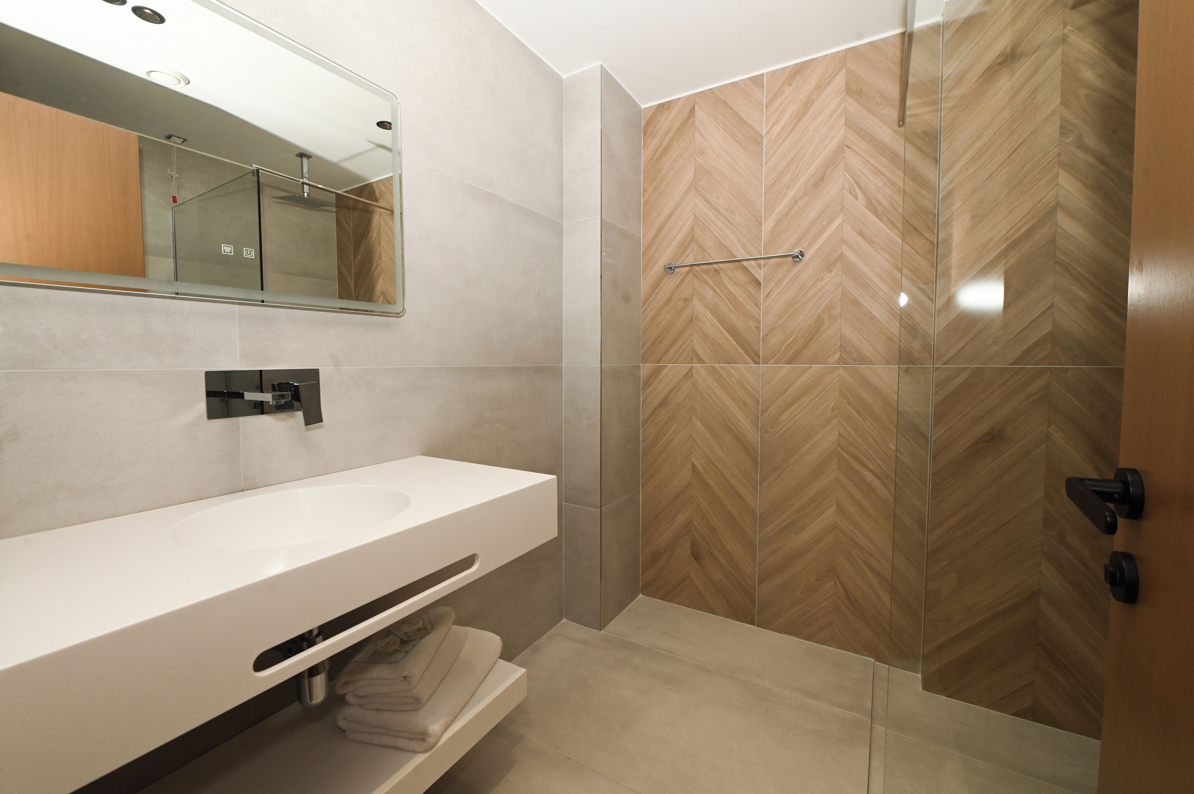 A modern bathroom with a white sink, a mirror, and a shower area with a herringbone wood pattern wall.