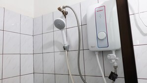 Een hoek van een badkamer met een betegelde muur, een handdouche en een aan de muur bevestigde boiler.