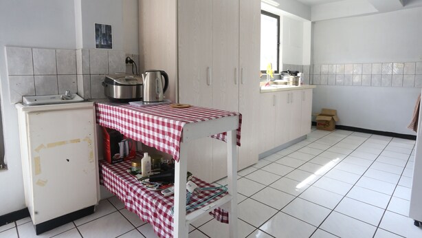 Een keuken met een rood-wit geruit tafelkleed, een waterkoker en een draagbaar gasfornuis.