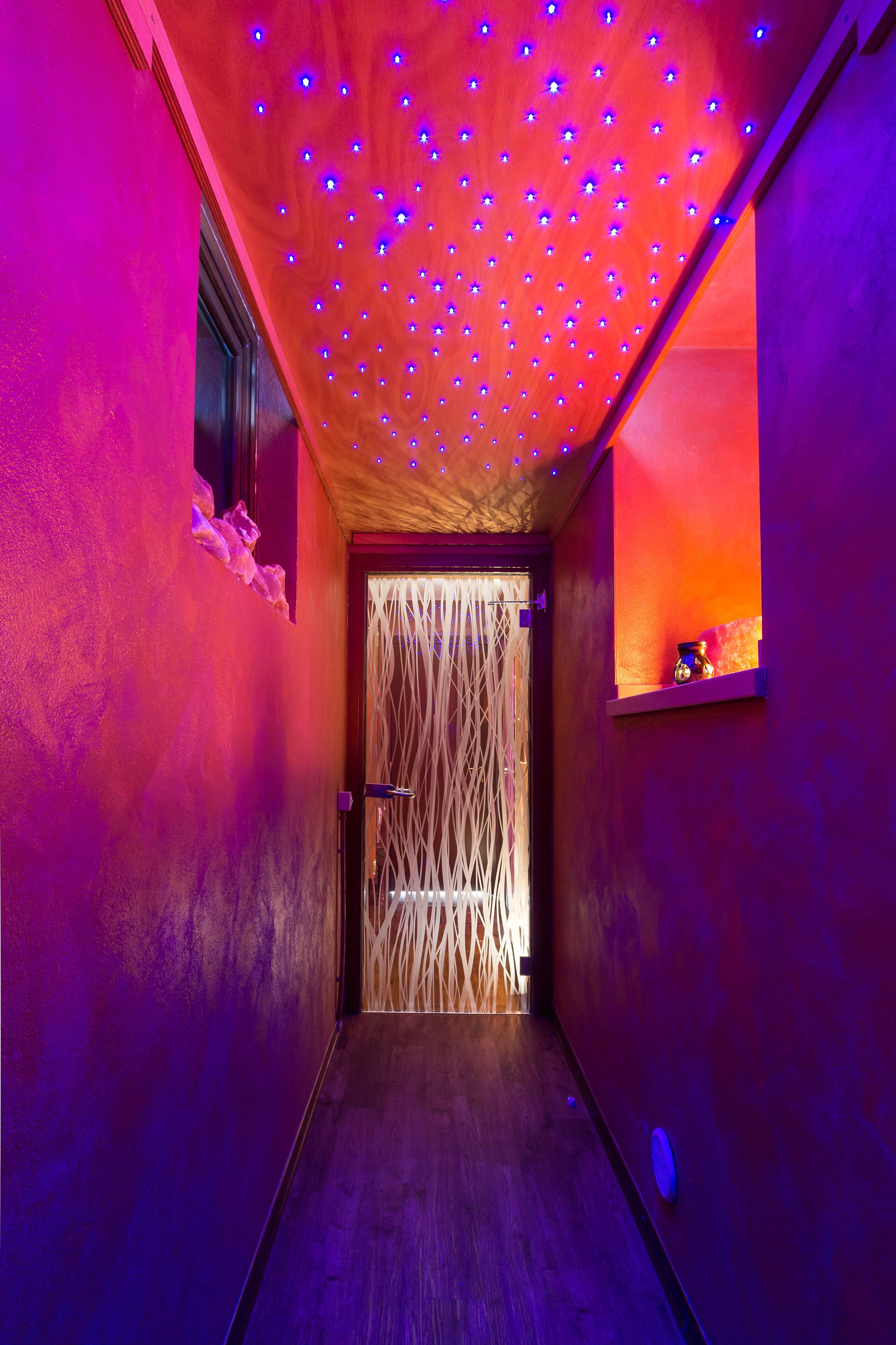 A narrow hallway with a wooden floor, a textured wall, and a door with a woven design.