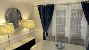 A dining area with a marble table, four chairs, two lamps, a decorative mirror, and a window with blue curtains. - Stunning 4-bed House in Rochester (Rochester)