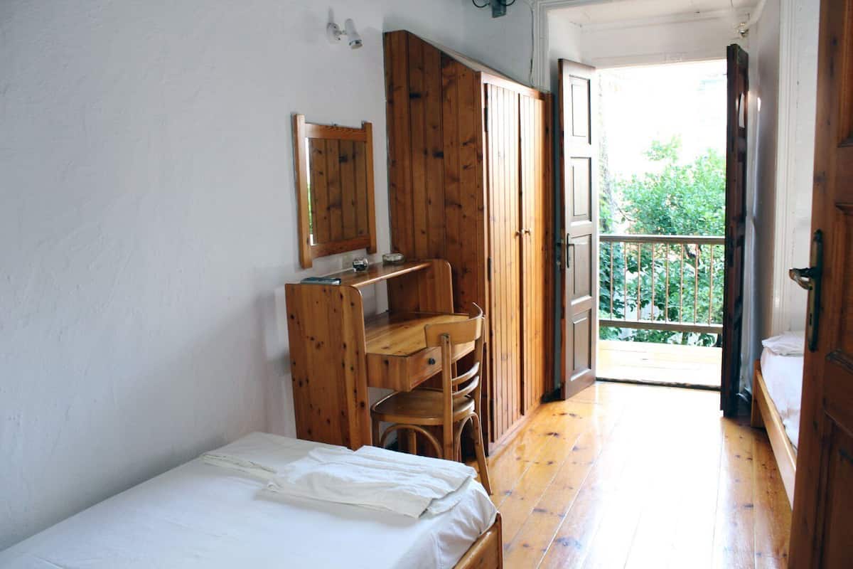 A bedroom with a wooden bed, a desk, and a wardrobe. There is a balcony with a railing.